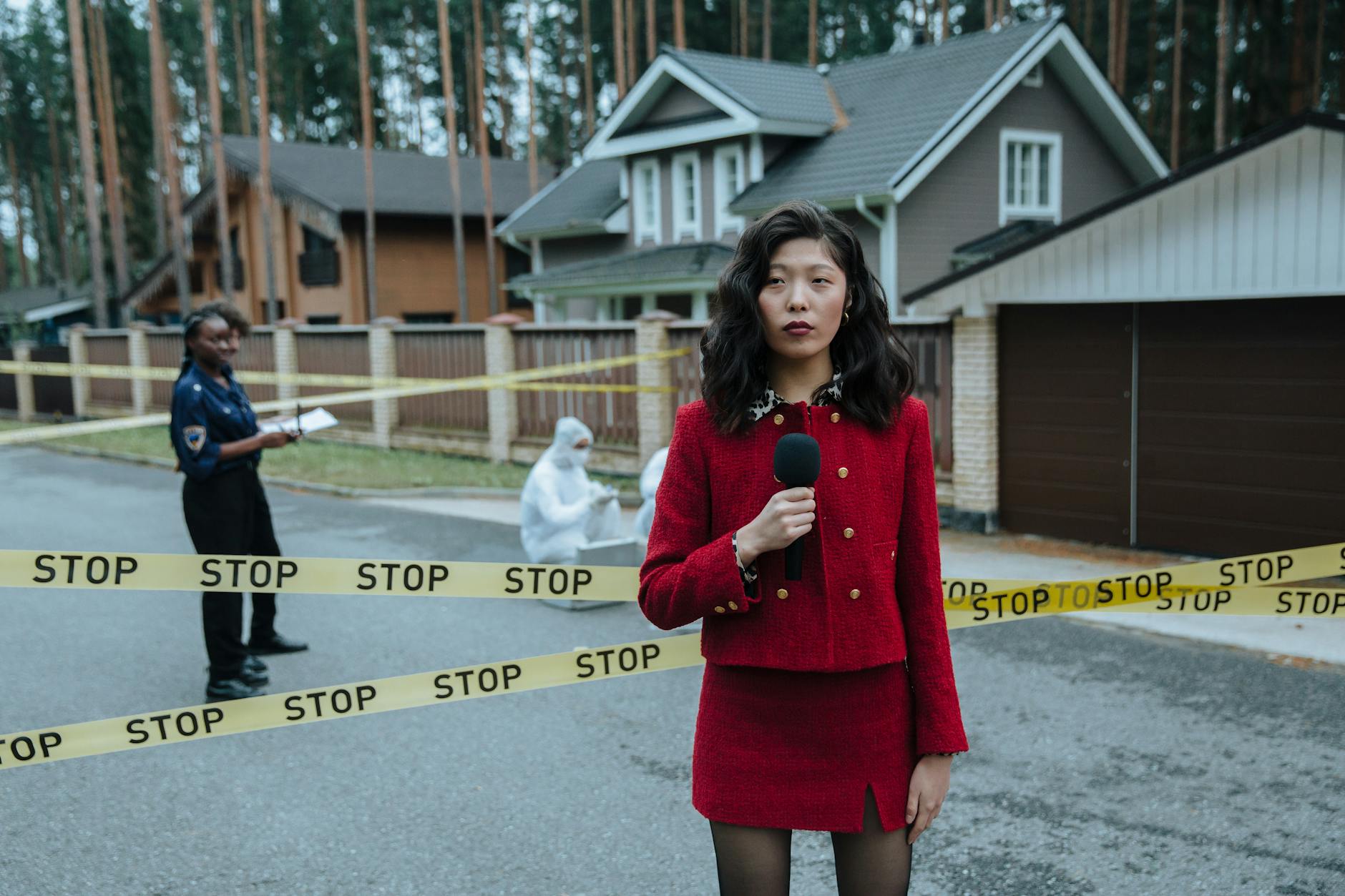 A journalist in a red outfit reporting live from a crime scene outdoors with stop tape and police presence.