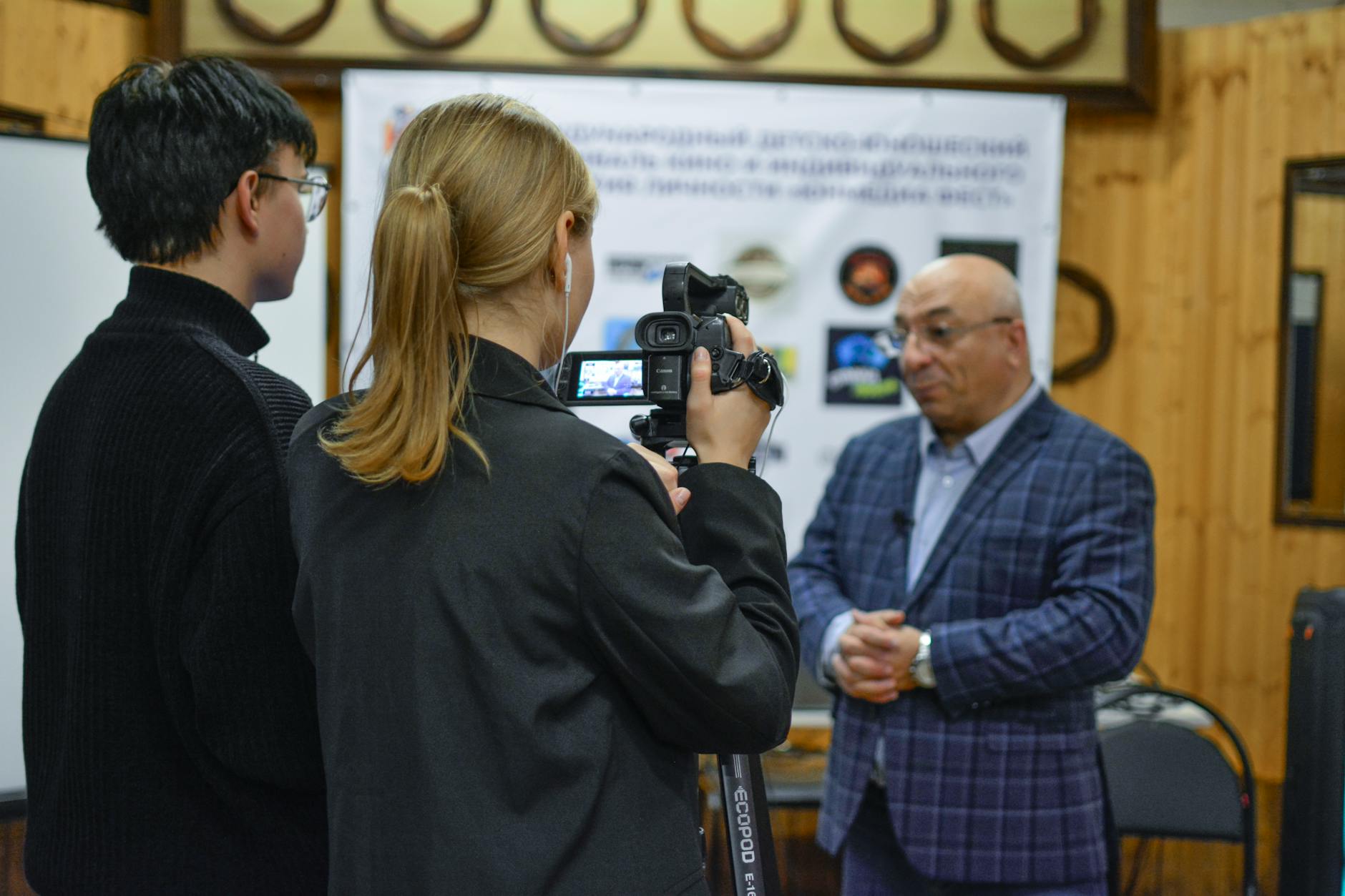 A journalist records an interview with a man using a camcorder indoors.
