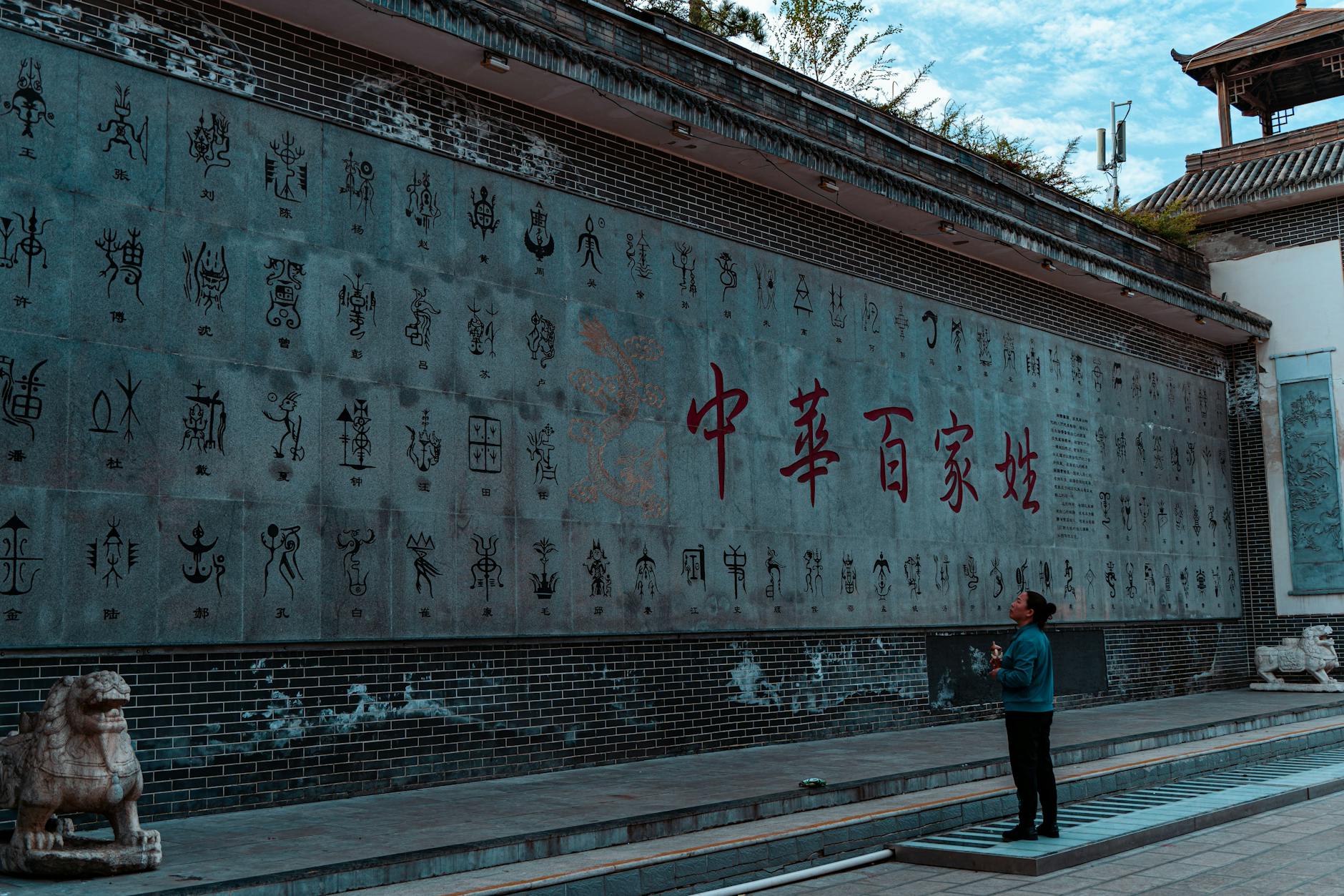 A person admires an ancient Chinese script wall outdoors.