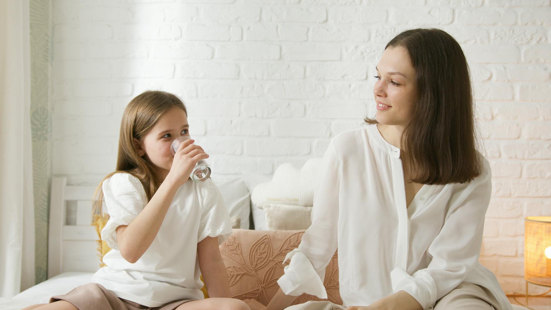 Smiling mother and daughter sitting together at home in a cozy bedroom, sharing a special moment.